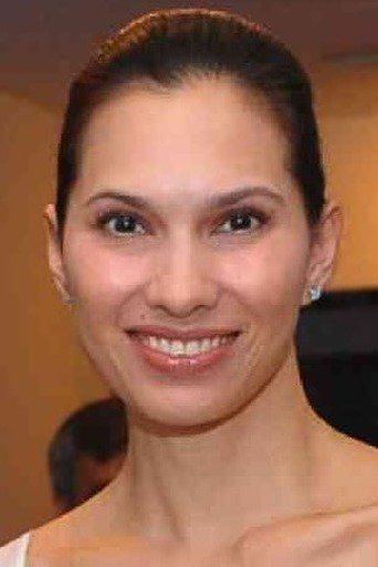 Nanette Medved smiling with a ponytail hairstyle and wearing a white dress.