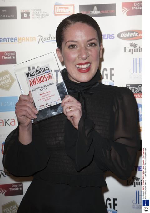 Natalie Casey smiling and wearing a black dress while holding a plaque.