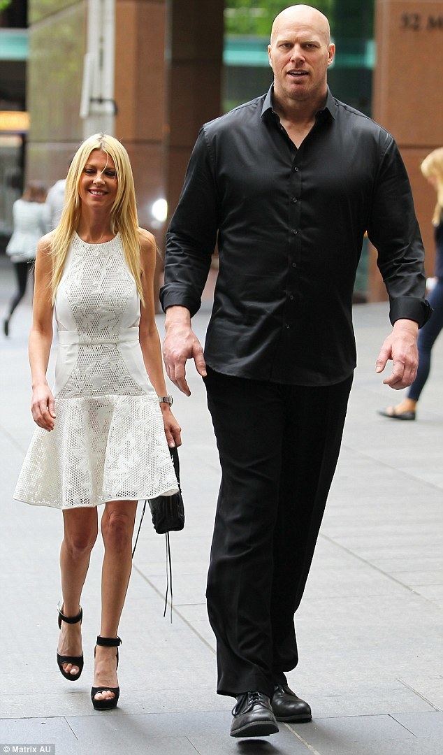 Tara Reid, smiling while walking on the street with Nathan Jones. Tara has blonde hair down, carrying a bag, and wearing a white dress, a wristwatch, and black heels while Nathan is wearing a black long sleeve, black pants, and black formal shoes