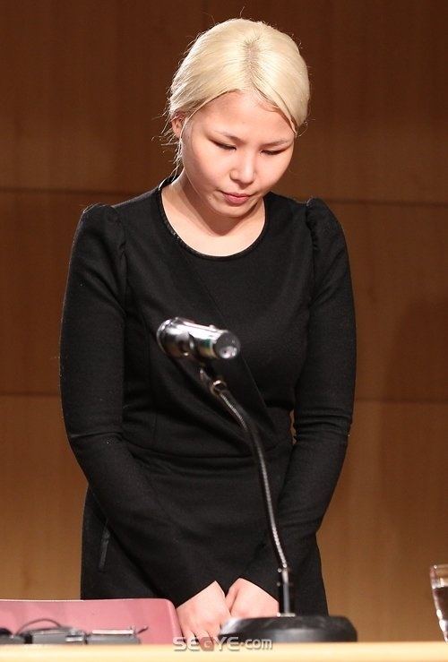 Ali standing and apologizing in a press conference for her song, “Nayoungee” which mentions Nayoung’s 2008 rape incident and wearing a black dress