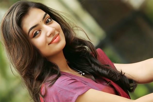 Nazriya Nazim smiling closed mouth with wavy hair and a bindi on her forehead and wearing a pink saree.
