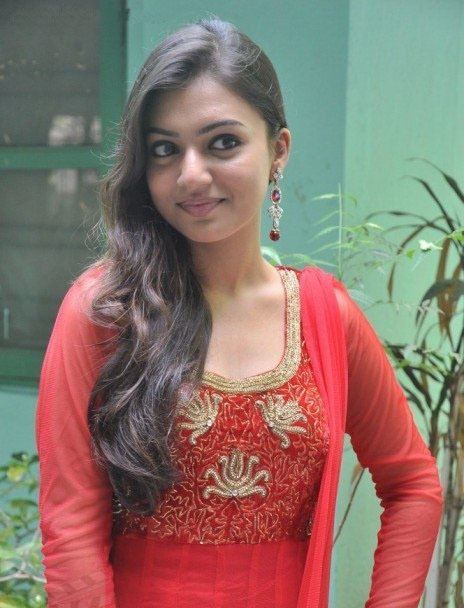 Nazriya Nazim posing and smiling closed mouth while wearing a red and gold Mekhela Sador and an earring.