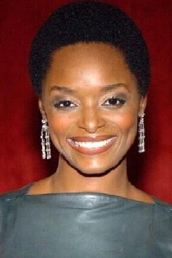 N'Bushe Wright smiling while wearing a gray blouse and earrings