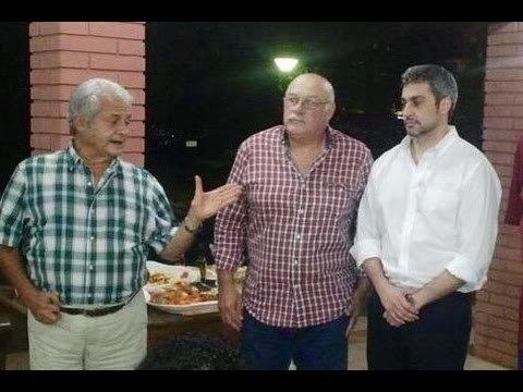 From left Ángel Roberto Seifart is serious, mouth half open talking with two men, his right hand holding his belt, left hand up open pointing in his left, has white hair wearing brown watch white long sleeve under a blue checkered long sleeve polo and white pants. In the middle is a man standing, with his hands down has white bald hair and a mustache wearing red checkered long sleeve, eyeglasses and blue pants, at the right is a man standing with his two hand crossed together below his belly has beard, mustache, and a black hair wearing white long sleeve polo and black pants.
