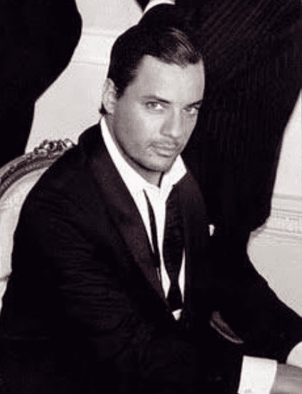 Nick Kamen wearing black coat and white long sleeves while sitting on a chair