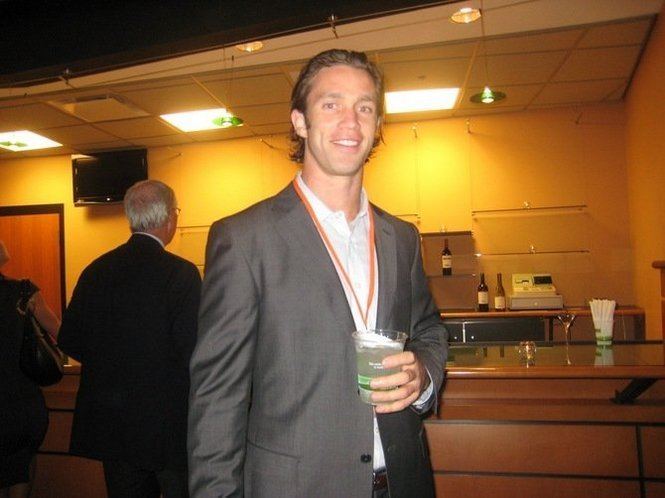 Nick Sorensen holding his drinks with the smile while wearing gray coat and white long sleeves