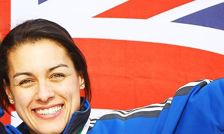 Nicola Minichiello smiling while the Flag of the United Kingdom is in the background and she is wearing a blue jacket and earrings