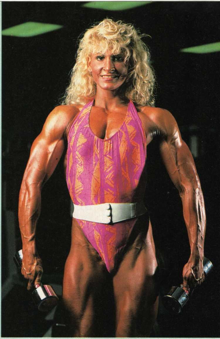 Nikki Fuller smiling while carrying a dumb-bell and wearing a pink and orange swimsuit with a white belt