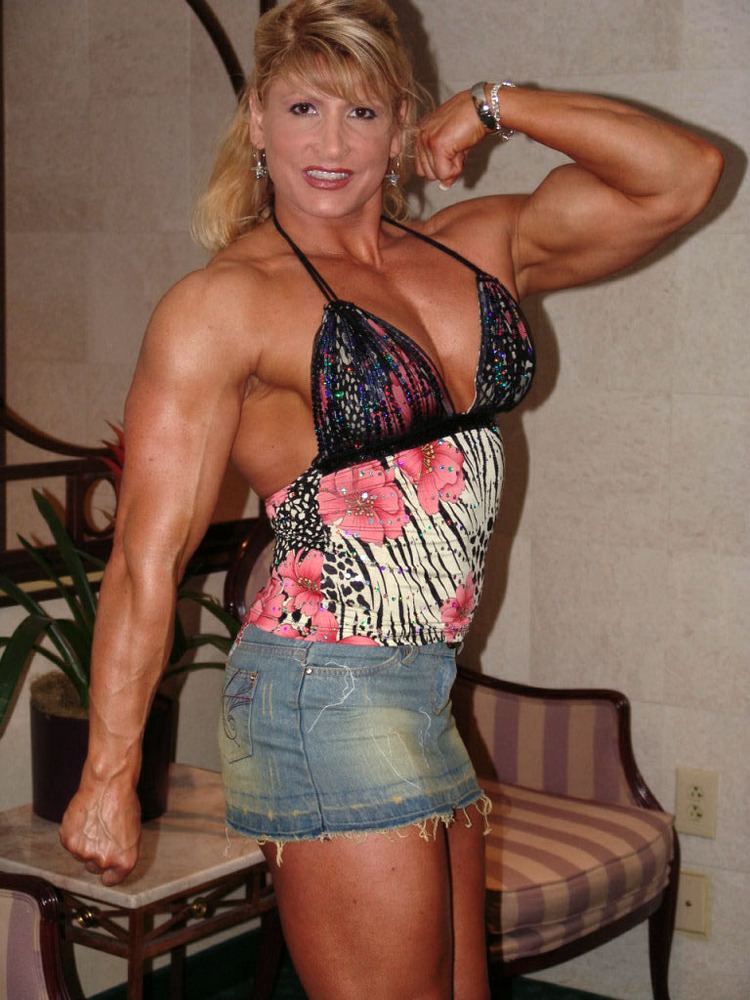 Nikki Fuller smiling while showing her muscle while wearing a black and pink floral top and denim skirt