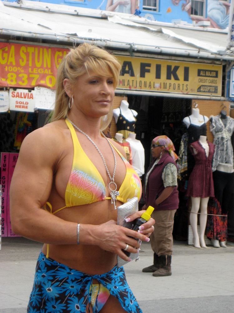 Nikki Fuller smiling and holding a gray wallet and bottle while wearing a yellow, pink, and blue bikini