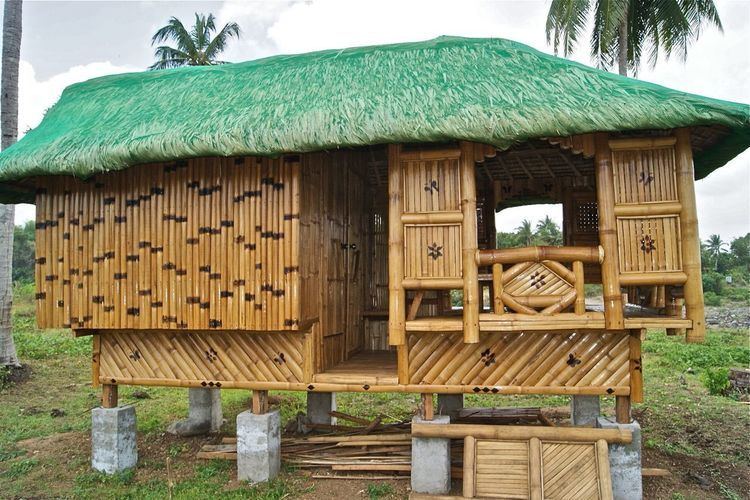 A modern nipa hut with a green net on the roof and with cement post.