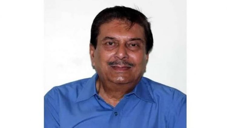 In a white background, Nipon Goswami is smiling, has black hair and a mustache wearing a blue polo shirt.