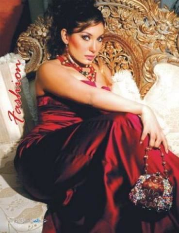 Nirma sitting on the chair while holding a clutch bag and wearing a red gown