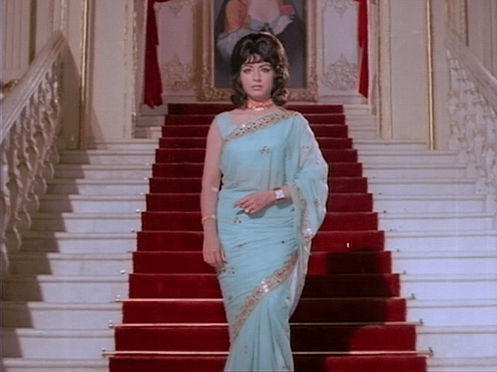 A scene from "Ganwaar" (1970) featuring Nishi as Mrs. Rani Rai wearing a light blue dress while walking down the stairs