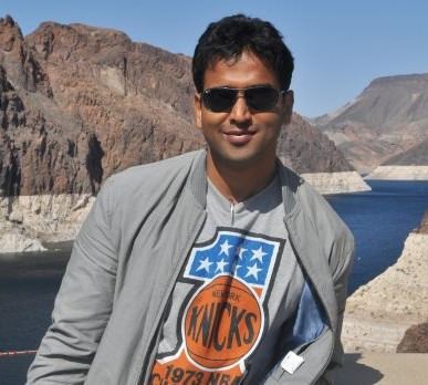 Nithin Kamath at Hoover Dam, wearing sunglasses, a gray jacket, and a gray shirt printed with a ball and stars.