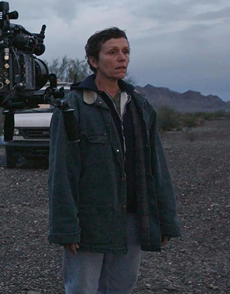 Frances McDormand looking afar while wearing a blue jacket and denim jacket on the set of the 2020 American drama film, Nomadland