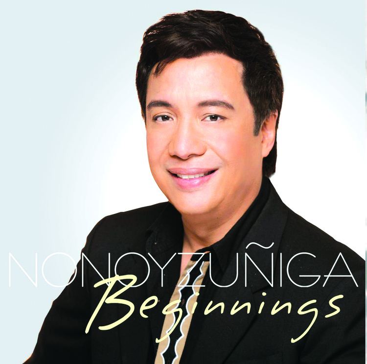 Nonoy Zuniga smiling while wearing a black coat over a black formal attire on the cover of his album Beginnings.