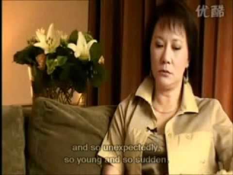 Nora Miao with a sad face and sitting on a sofa during an interview, wearing a brown blazer over a brown tube top.