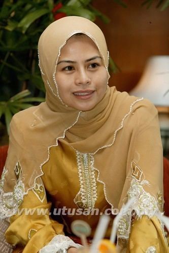 Noraini Ahmad smiling while wearing a brown hijab with white lace and a mustard long sleeves dress