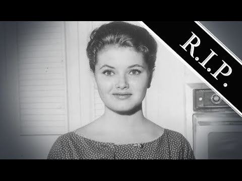 Noreen Corcoran is smiling, and has black hair, behind her (on left) is a stove oven, and on the upper right is the word R.I.P, she is wearing a black dress with white design.