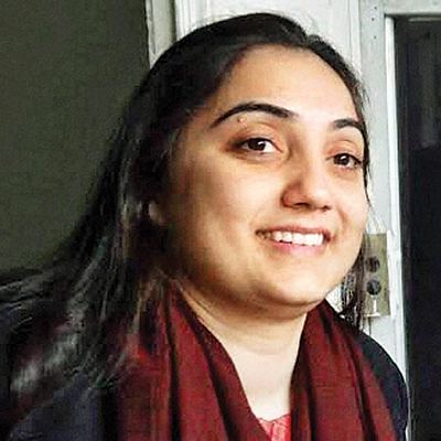 Nupur Sharma is smiling with her black hair wearing a maroon scarf around her neck and a red shirt under a black cardigan