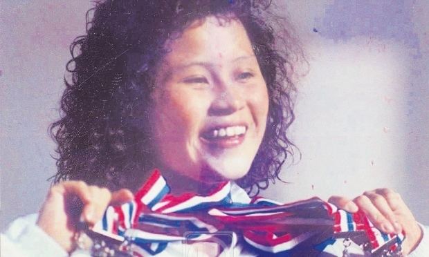 Nurul Huda Abdullah smiling while flexing her medals and wearing a white jacket