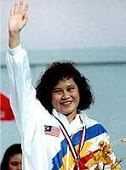 Nurul Huda Abdullah smiling while waving her hand and wearing a medal and white, blue, and yellow jacket