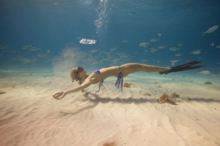 Ocean Ramsey swimming, wearing goggles, a blue two-piece, and scuba fins.