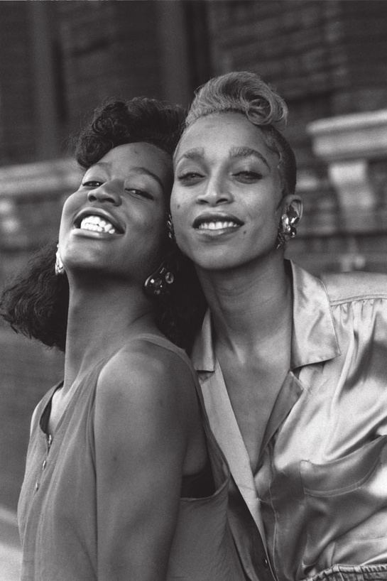 Temperance St. Laurent (left) is smiling and has black hair, wearing black earrings, and a black bra under a brown sleeveless top. Octavia St. Laurent (right) is smiling and has black hair, a mole on her right cheek and lower left cheek, wearing silver-black earrings, and a gray silk top with a pocket on right.