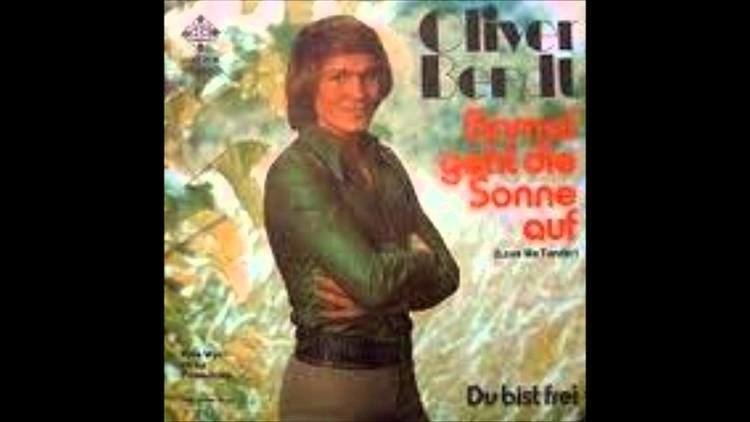 Oliver Bendt smiling while wearing green long sleeves and brown pants on the album cover of "Einmal Geht Die Sonne Auf"