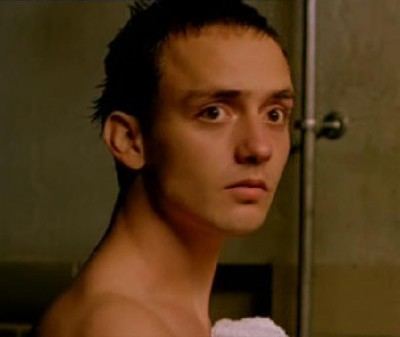 Oliver Loftéen inside a bathroom and looking at something while holding a towel.