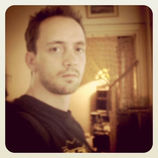 Oliver Loftéen posing inside his house wearing a black shirt and having thin facial hair.