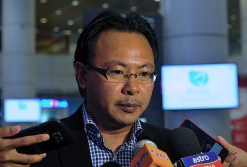 Ong Kim Swee, in one of his interviews, wearing eyeglasses, blue checkered long sleeves, and a black coat