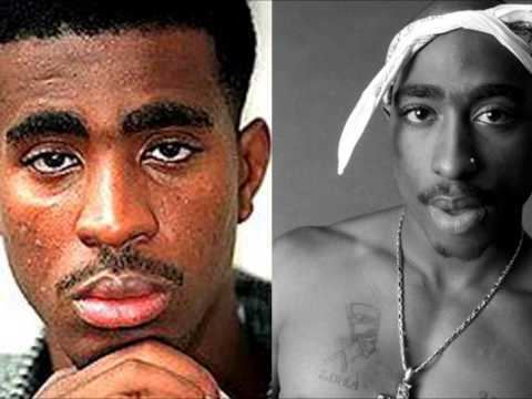 On the left, Orlando Anderson with a serious face while his hand is on his chin, with a mustache and wearing a green and white checkered polo shirt. On the right, Tupac Shakur is topless with a serious face, a mustache, a tattoo on his body, a nose ring, wearing a white cloth on his head, and a cross necklace.