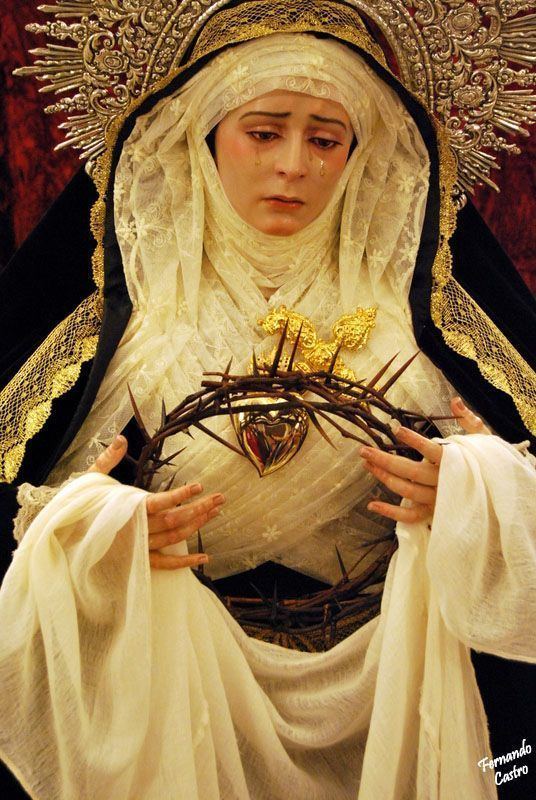 Our Lady of Sorrows statue crying while holding the crown of thorns and a dagger pierced into her heart while wearing a black and gold veil