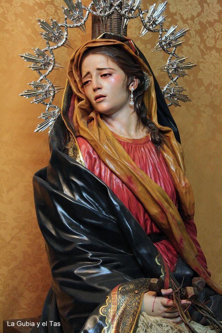 Our Lady of Sorrows crying with blood on her hand while holding the crown of thorns and wearing a black and yellow veil and red dress