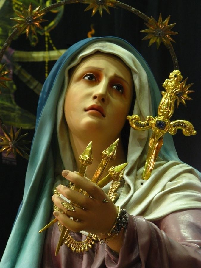 Our Lady of Sorrows statue with a dagger pierced into her heart while wearing a blue and white veil and purple long sleeve dress