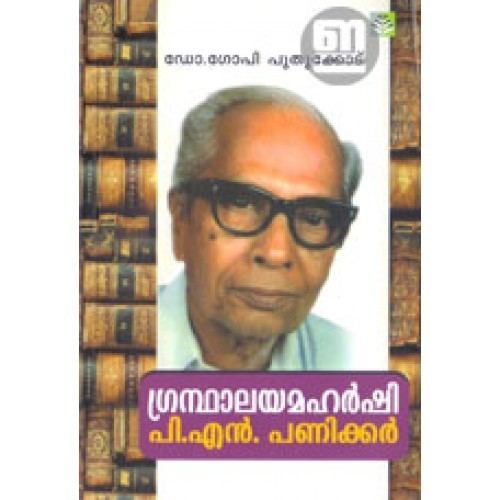 P N Panicker smiling with his gray hair and a phrase below “പി.എൻ. “ and books in the background and he is wearing black eyeglass and a blue polo