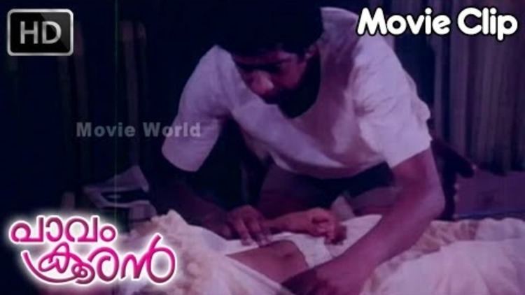 In the movie scene Paavam Krooran 1984, Captain Raju standing looking down, trying to unbutton a dress of a woman while asleep, has black hair wearing white top, a girl sleeping on bed wearing white top and pants.