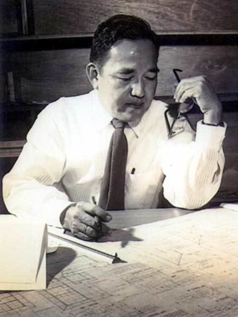 Pablo Antonio holding a ballpen and eyeglasses while looking at the architectural plan and wearing long sleeves and a necktie