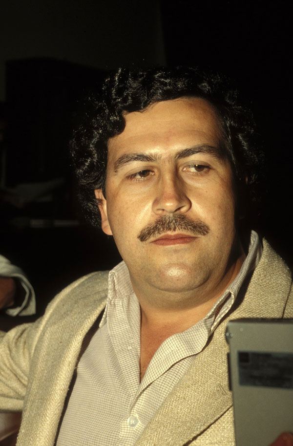 Pablo Emilio Escobar Gaviria with a mustache, curly hair, and wearing a suit.