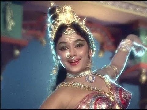 Padmini smiling while wearing a glamorous dress, nose-jewel, headdress, necklace, and bracelets