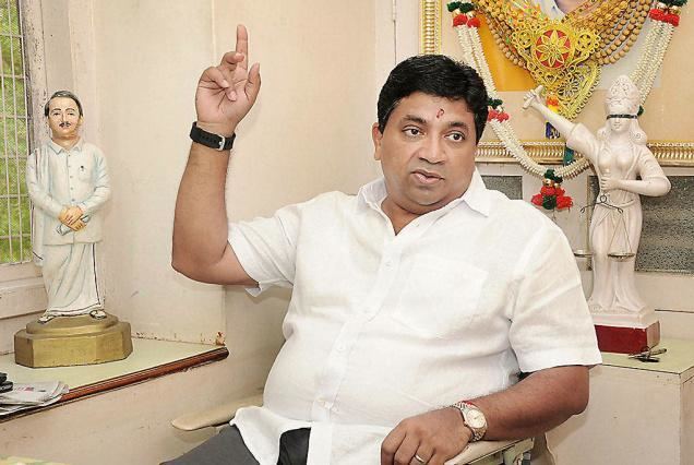 Palanivel Thiagarajan wearing white polo and wristwatch pointing his fingers upward