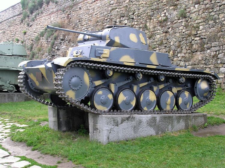 A gray and yellow Panzer II on top of concrete cement beside a gray light tank.