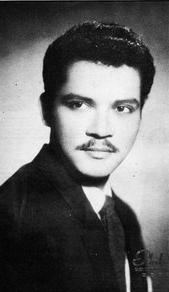 Paquito Diaz with mustache while wearing a black coat, long sleeves, and necktie