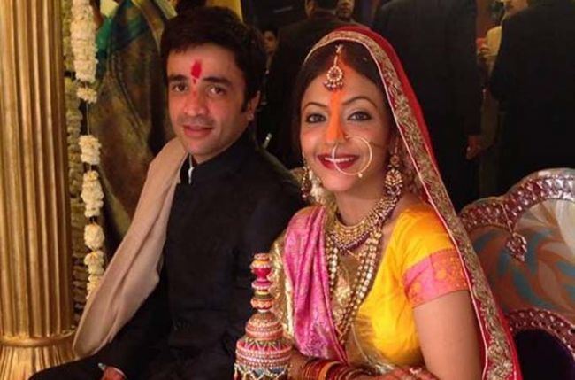 Puneet Sachdeva and Pariva Pranati are smiling during their wedding ceremony while Pariva is wearing a gold and red veil, pink and yellow dress, and jewelry