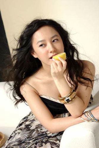 Park Joo-mi with curly black hair, wearing a sexy dress while holding an orange.