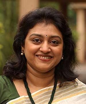 Parvathy Jayaram is smiling, has black hair and a bindi on her forehead, wearing silver earrings, a green necklace, a green blouse, and a light-colored saree.