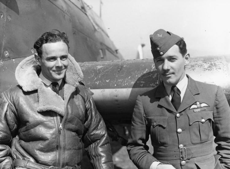 Pat Pattle smiling with George Rumsey and standing by a Hawker Hurricane aircraft at Larissa in Greece with Pat wearing a coat while George wearing a pilot uniform and a hat