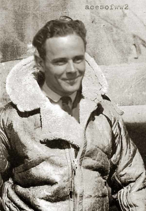Pat Pattle smiling and standing by the Hawk Hurricane aircraft and wearing a coat